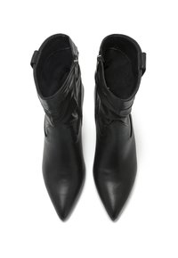 Botas negras de ankle hechas de cuero liso, con punta afilada, diseño holgado y cierre de cremallera lateral. Forro interior suave.