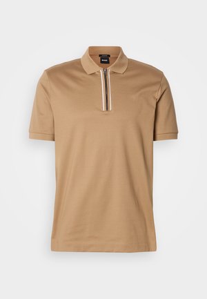 Polo shirt beige en tissu lisse, avec un col zippé à mi-hauteur, des manches courtes et des détails de fermeture éclair contrastants en blanc et noir.