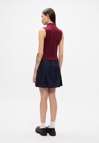 Un haut polo sans manches bourgogne associé à une jupe patineuse en denim bleu. La tenue comporte un col et des détails de couture, avec des chaussures noires et des chaussettes blanches.