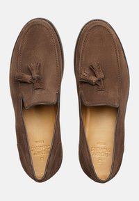 Mocassini in suede marrone con una superficie liscia, dotati di un accentuato pon-pon decorativo, punta aperta e un design semplice e facile da indossare.
