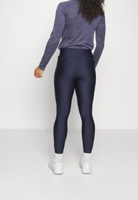 Granatowe, wysokie leginsy z elastycznego materiału, o gładkiej teksturze i dopasowanym kroju, zestawione z białymi trampkami i skarpetkami.