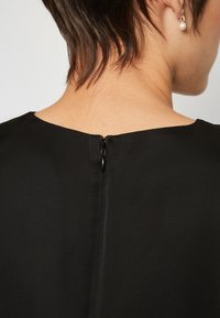 Indumento in tessuto nero con scollatura rotonda e zip nascosta sul retro, che presenta una texture liscia e una finitura delle cuciture pulita.