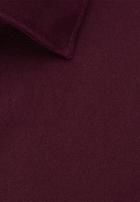 Bordeauxfarbener Stoff mit glatter Textur, der einen umgeschlagenen Kragen aufweist. Die Oberfläche ist einheitlich ohne sichtbare Muster oder Verzierungen.