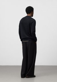 Svart tröja med rund hals och långa ärmar, kombinerad med lösa svarta byxor. Slät textur, minimalistisk design, utan synliga mönster.