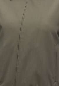 Κοντινή λήψη ελιτζί πράσινου υφάσματος με ορατό ραφτό και μερικώς ανοιχτό φερμουάρ που εκτείνεται κάθετα κοντά στο κέντρο.