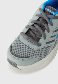 Baskets de sport en maille grises avec une surface texturée, lacets gris foncé, accents bleus et une conception à bout rond, dotées d'un col rembourré.