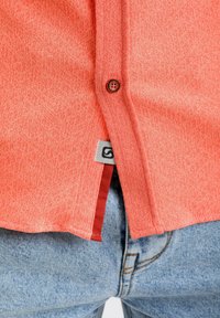 Koraaltextuur shirt met knoopsluiting, met een labelsteekdetail, gedragen over blauwe denim jeans.