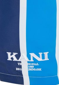 Kék és tengerészkék csíkos fürdőnadrág fehér részletekkel, hímzett "KANI" logóval. Simává és könnyű anyagból készült.