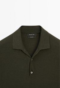 Polo shirt in cotone verde scuro con colletto, caratterizzato da due bottoni e texture a coste sul colletto e sulle maniche.