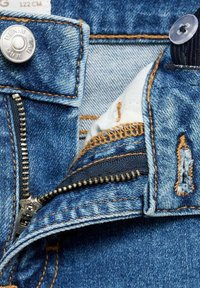 Plava traper tkanina sa svijetlim pranjem, uključujući srebrnu dugmad, zatvarač i narančaste šavove. Vidljiva izložena unutarnja podstava.