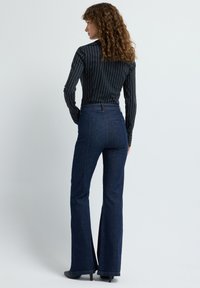 Džínové kalhoty s vysokým pasem a rozšířenými nohavicemi v tmavě modrém denimu s viditelným prošíváním. Kombinovány s černobílým pruhovaným tričkem s dlouhým rukávem.