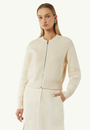 Cream knitted bomber jacket with a round neckline, front zipper, and ribbed hem. Features long sleeves and a smooth texture.
