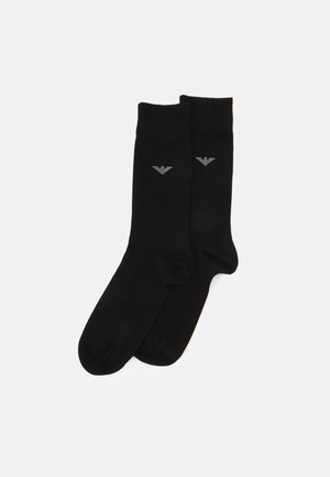 Chaussettes noires en tissu doux arborant un logo discret en gris sur un côté. Elles présentent un design classique avec une bordure côtelée.