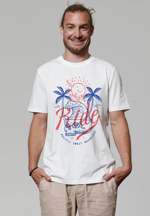 Witte katoenen T-shirt met een kleurrijk graphic ontwerp van palmbomen, een zon, en het woord "Ride" in vette rode en blauwe letters.