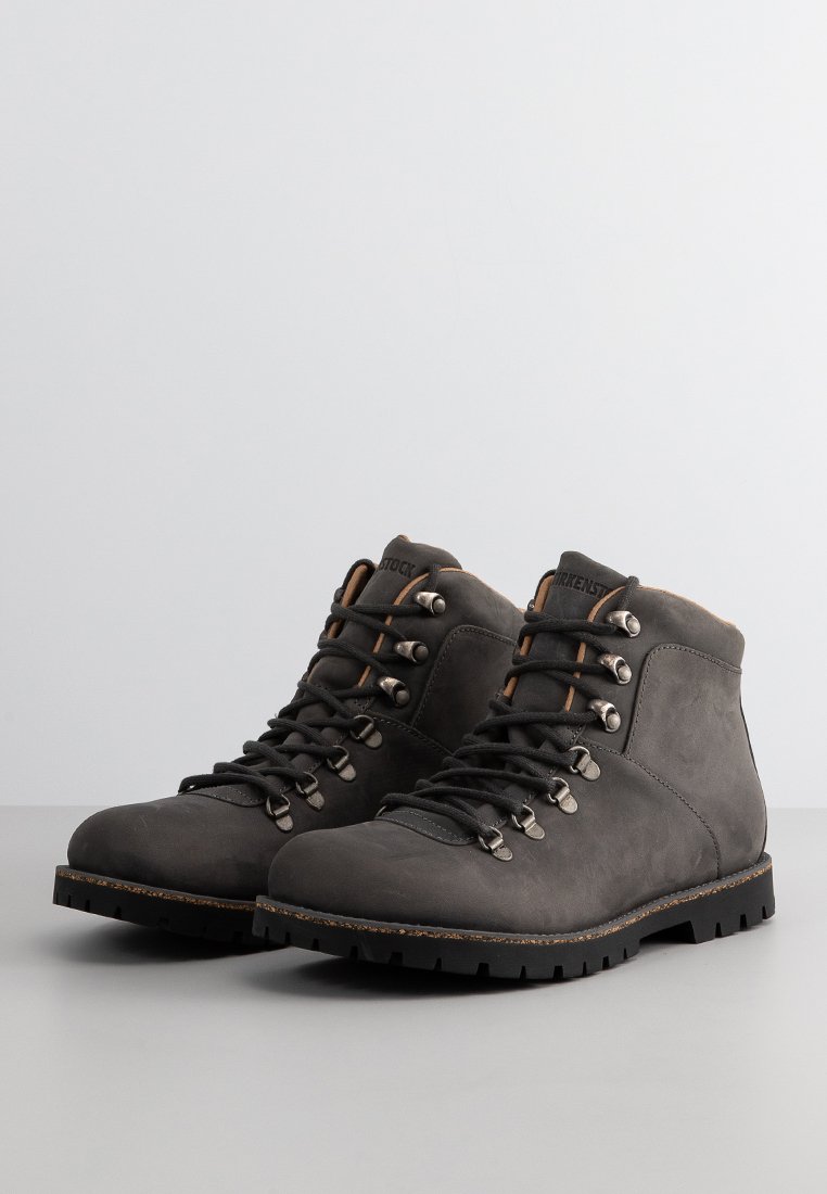 Graue Wanderschuhe aus Leder mit hohem Knöchel, strukturierter Oberfläche, Metallösen und kontrastierenden braunen Akzenten an der Zunge und Sohle.