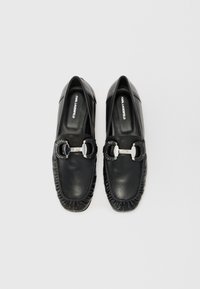 Sorte lær loafers har en dekorativ sølvspenne og rynkerundt kantene. Indre logo er synlig.