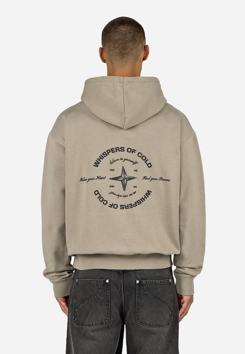 Felpa beige con cappuccio e cordino, caratterizzata da una stampa grafica sul retro che include una bussola e testo in nero. Texture del tessuto morbida.