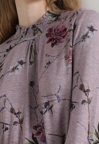 Långärmad lila topp med blommönster i rosa, grönt och blått. Rynkad nacke med mjuk tygkänsla.