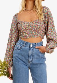 Blommig crop top med puffärmar och en samlad design i pastellfärger. Matchad med högmidjade, ljusblå jeans i denim.