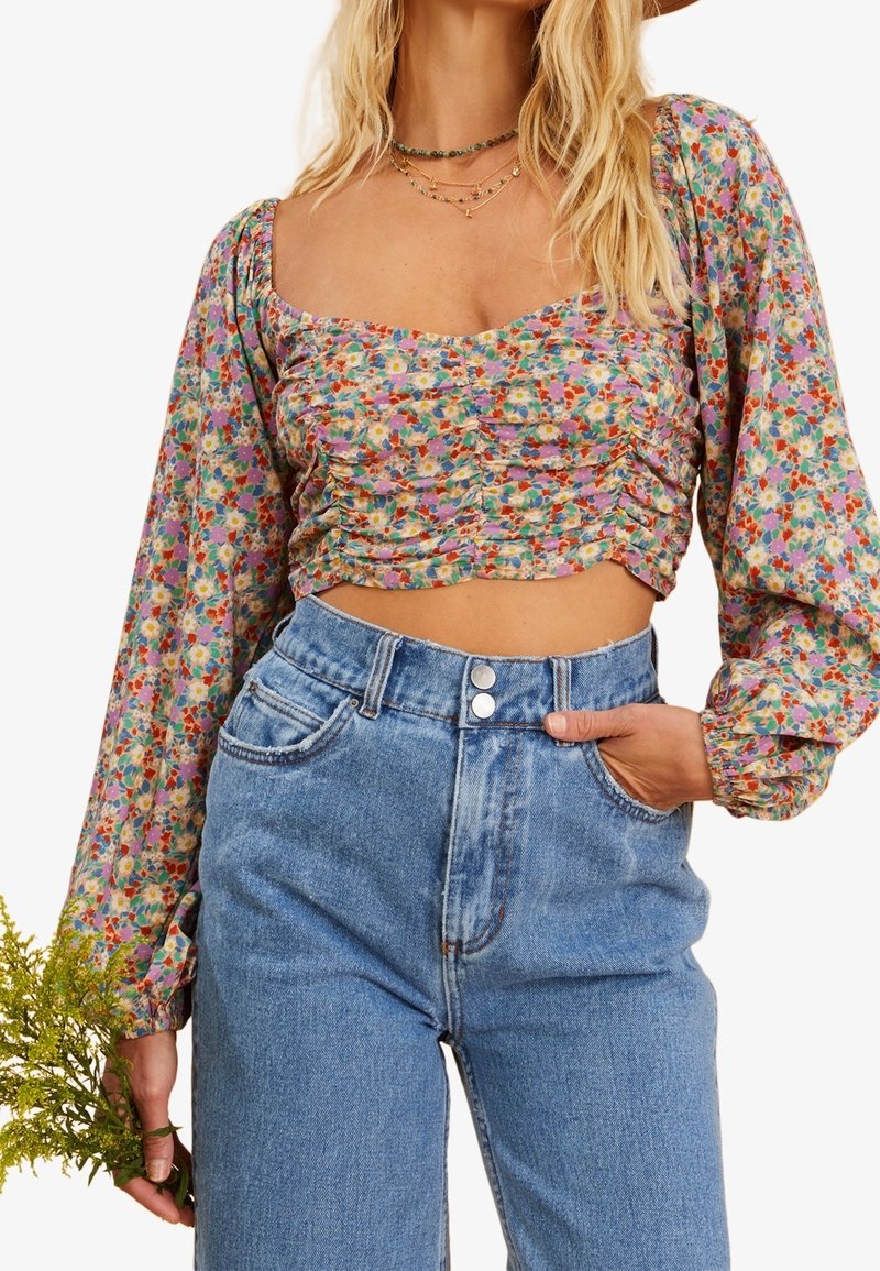 Blommig crop top med puffärmar och en samlad design i pastellfärger. Matchad med högmidjade, ljusblå jeans i denim.