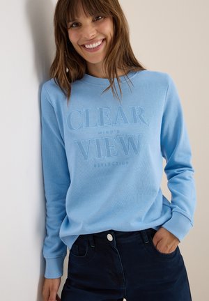 Felpa azzurro chiaro con collo rotondo, caratterizzata da lettere texturizzate "CLEAR VIEW" e "REFLECTION". Abbinata a jeans di denim scuro.