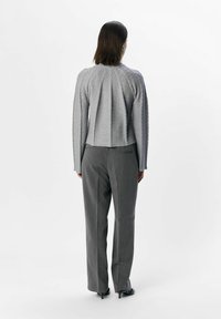 Grauer Pullover mit gerippter Textur und gefaltetem Rücken, kombiniert mit grauen maßgeschneiderten Hosen und schwarzen High Heels.