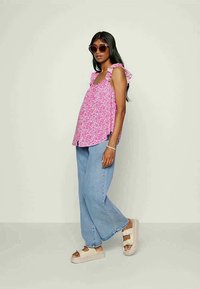 Top floral rosa sem mangas com alças em babados, combinado com jeans de perna larga azul claro e sandálias de plataforma bege. Óculos de sol castanhos usados.