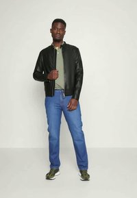 Svart lærjakke, olivengrønn polo skjorte, blå jeans og grønne joggesko. Jakken har glidelås og en tettsittende design.