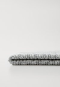 Couverture en tricot grise soigneusement pliée, présentant une texture côtelée et des fibres douces, avec un bord lisse pour un aspect propre et fini.