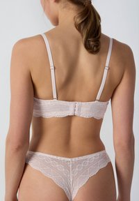 Koronkowy biustonosz i pasujące stringi w delikatnym różowym kolorze. Regulowane ramiączka, zapięcie na haczyk oraz delikatne wykończenie wzdłuż brzegów.