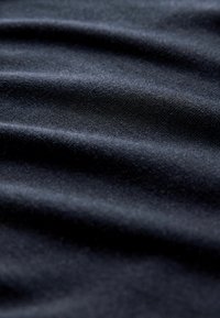 Svart tyg med en slät textur, som visar subtila vågor och fina vävdetaljer. Materialet verkar mjukt och lätt.