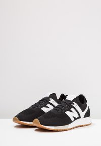 Scarpe sportive in bianco e nero con tomaia in maglia, suola bianca e suole color gomma posizionate affianco su una superficie bianca.