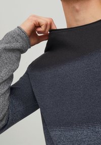 Langärmliger Pullover mit einem strukturierten grauen Körper, schwarzem Kragen und dunklem Verlaufsmuster. Der Kragen wird mit einer HandAdjusted.
