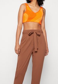 Oranje gebreide crop top met een V-hals en abstract patroon, gecombineerd met hooggewaisted bruine pantalons met een strikriem.