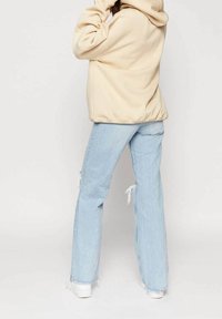 Felpa beige in pile con vestibilità rilassata, abbinata a jeans azzurri strappati con orlo sfilacciato e design a gamba dritta, indossata con sneaker bianche.