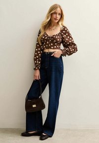 Brun prickig crop top med puffärmar, högmidjade mörk denim vida byxor och en liten brun väska med texturerad yta.