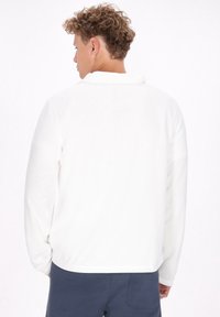 Hvid fleece pullover med ståkrave, lange ærmer, afslappet pasform og en glat tekstur. Begrænset synlig syning og ingen mønstre.