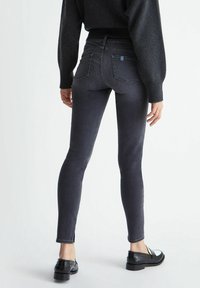 Vaqueros de denim negros ajustados con cintura alta, que cuentan con dos bolsillos traseros y detalles de costura. Se llevan con un suéter de punto oscuro y mocasines brillantes.