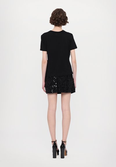 Schwarzes kurzärmliges T-Shirt, kombiniert mit einem schwarzen, mit Pailletten besetzten Minirock. Der Rock hat ein strukturiertes Muster, und das Model trägt High Heels.