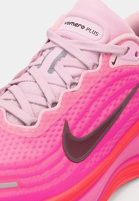 Rosa Nike Vapormax Plus-sneaker med svart swoosh-logotyp, ljusrosa skosnören och texturerat ovandel visas i närbild.
