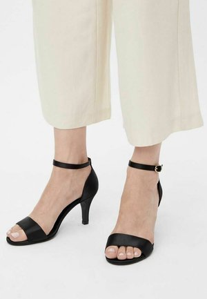 Czarne skórzane sandały na wysokim obcasie z paskami na kostce, odkrytym palcem, smukłą sylwetką i połyskującym wykończeniem.
