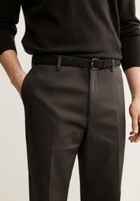 Pantalons taillés gris foncé avec une texture lisse, présentant une coupe droite, un pli subtil et une ceinture noire avec une boucle en argent.