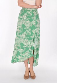 Fustă midi cu imprimeu floral verde și tiv evazat, având o fanta laterală. Materialul pare ușor și fluid. Asortată cu tocuri înalte bej.
