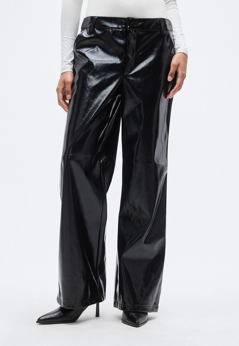 Μαύροι ψεύτικοι δερμάτινοι παντελόνες με φαρδιά γραμμή και γυαλιστερό φινίρισμα, με κλείσιμο με κουμπί μπροστά και πλαϊνές τσέπες. Συνοδεύονται από μυτερές ψηλές γόβες.