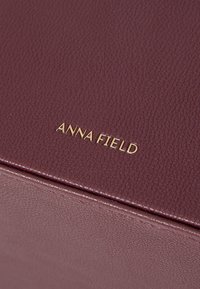 Burgundy textured leather box with a gold "ANNA FIELD" embossed logo. Features a smooth finish and clean, rectangular design.