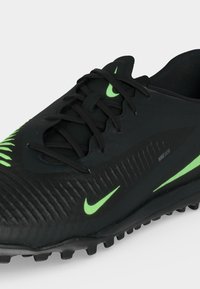 Μαύρο αθλητικό παπούτσι Nike με πράσινες λεπτομέρειες, υφασμένο άνω μέρος, δεμένα κορδόνια και λαστιχένιες εξογκώσεις στη σόλα για καλύτερη πρόσφυση.