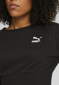 Top sportivo nero con scollatura rotonda, caratterizzato da un logo Puma bianco sulla parte sinistra del petto. Il tessuto è liscio e dalla vestibilità aderente.