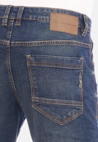 Jeans in denim blu scuro con etichetta in pelle marrone. Presentano una tasca posteriore con un logo stilizzato e cuciture a contrasto.