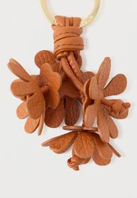 Δερμάτινο μπρελόκ με τέσσερα charms σε σχήμα λουλουδιού σε πλούσιο καφέ, διαθέτοντας υφή και χρυσό κυκλικό κρίκο για προσαρμογή.