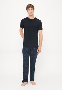 Svart kortermet t-skjorte kombinert med marineblå pysjamasbukser med et gjentagende grønt Lacoste-logo mønster. Enkel design, myk stoff.